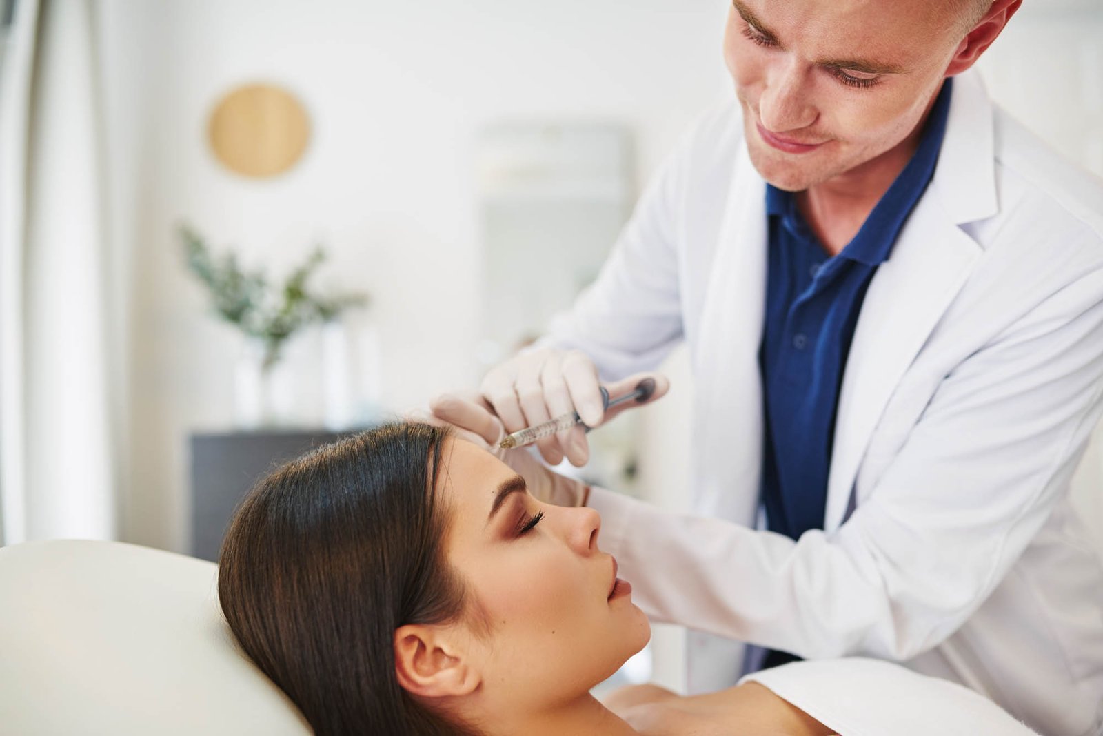 Doctor injecting botox into a female client’s forehead Smiling male doctor performing a botox injection to the forehead of a woman lying on a table in a beauty clinic