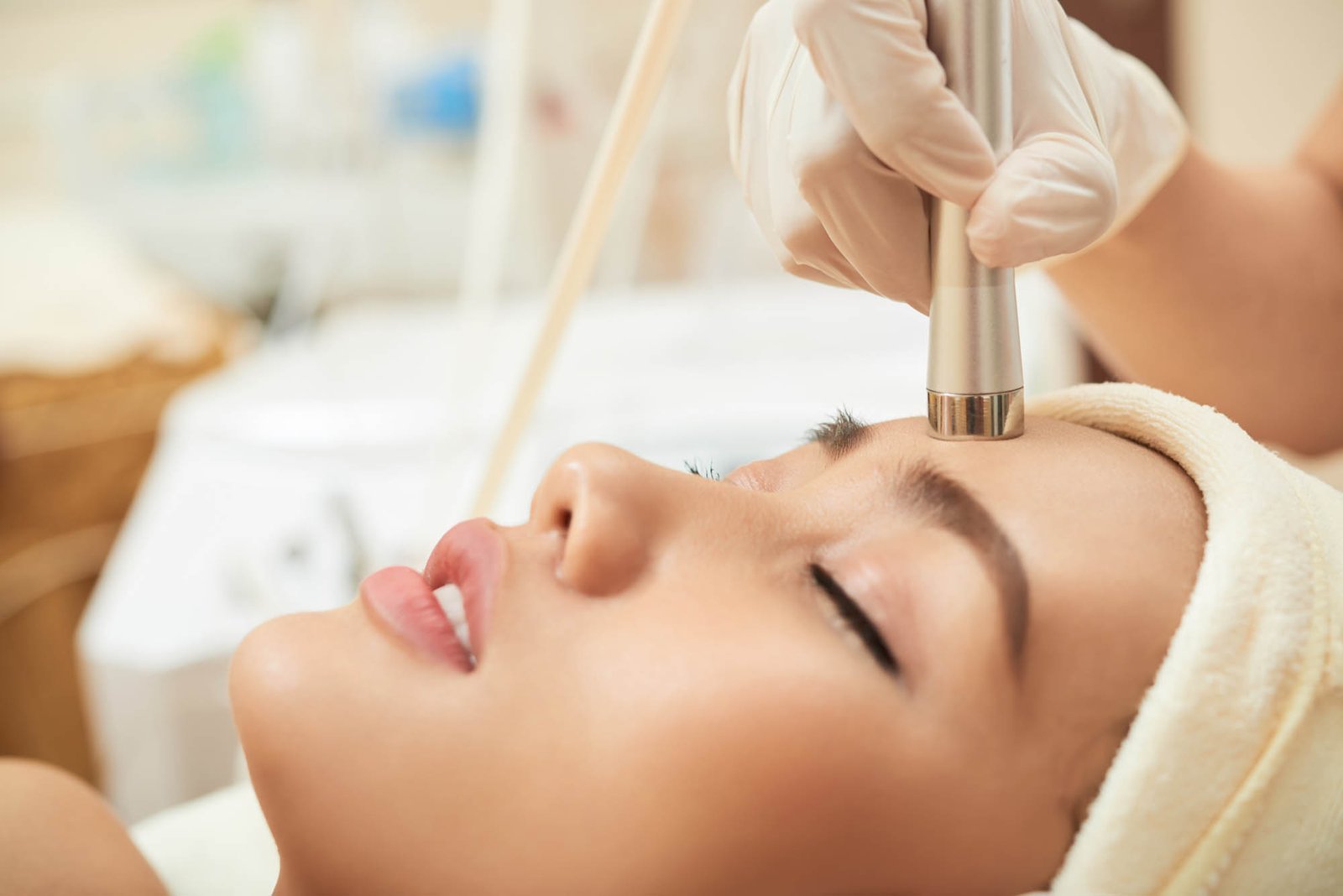 Enjoying Facial Massage Close-up shot of relaxed young woman lying on treatment table while highly professional beautician massaging her face with special equipment